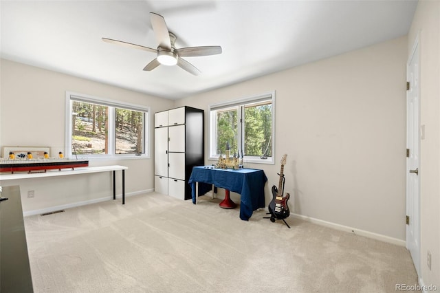 home office featuring healthy amount of natural light, ceiling fan, and light colored carpet