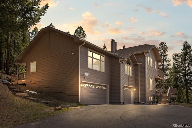 view of side of property featuring a garage, driveway, a chimney, and a wooden deck