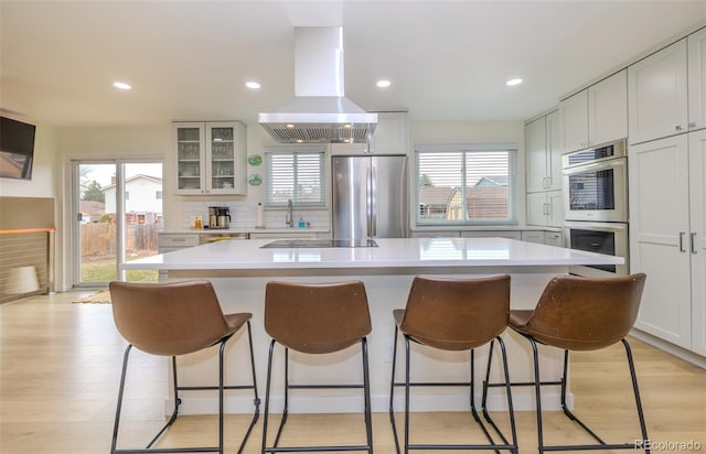 kitchen featuring a breakfast bar area, island range hood, stainless steel appliances, and decorative backsplash