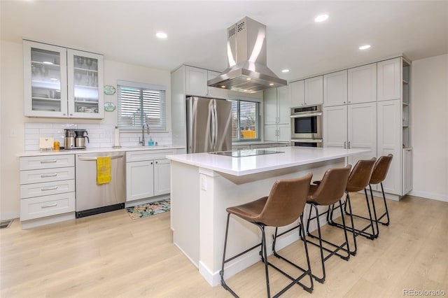 kitchen featuring a sink, light countertops, appliances with stainless steel finishes, tasteful backsplash, and island exhaust hood