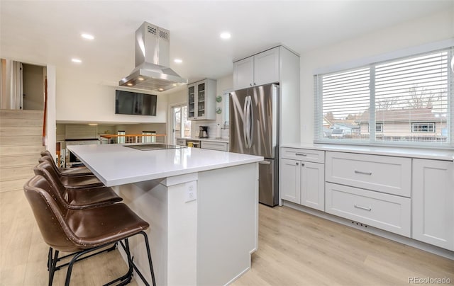 kitchen with a breakfast bar area, a kitchen island, light wood-style floors, freestanding refrigerator, and island exhaust hood