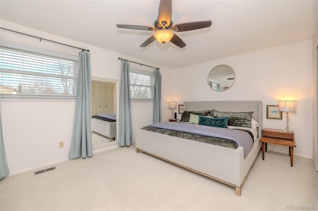 carpeted bedroom with a textured ceiling, visible vents, and a ceiling fan