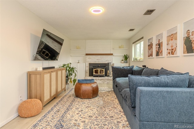 living area featuring light wood-style floors, visible vents, a textured ceiling, and baseboards