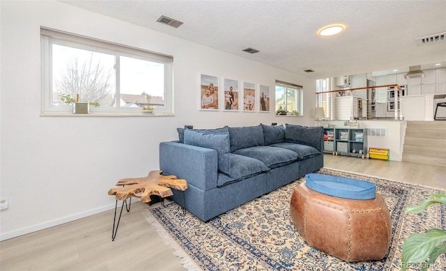 living room featuring stairs, visible vents, plenty of natural light, and wood finished floors