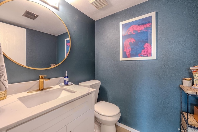 half bathroom with toilet, vanity, visible vents, and a textured wall