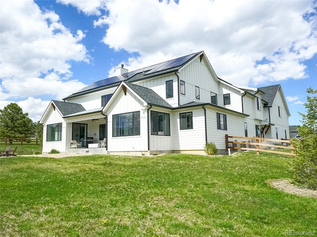 back of property with board and batten siding, a sunroom, a chimney, solar panels, and a lawn