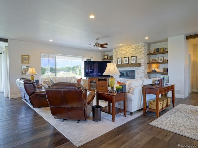 living room with dark wood-style flooring, a ceiling fan, baseboards, and a stone fireplace