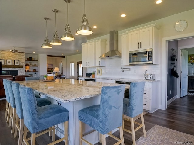 kitchen featuring wall chimney range hood, white cabinets, stainless steel microwave, and backsplash