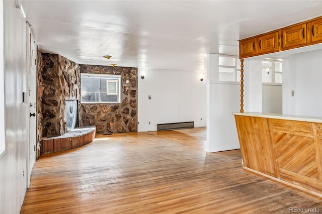 unfurnished living room featuring a stone fireplace, light wood-type flooring, and a baseboard heating unit