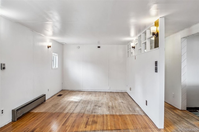 unfurnished room featuring hardwood / wood-style floors and a baseboard heating unit