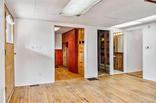 spare room featuring a paneled ceiling, wooden walls, and hardwood / wood-style floors