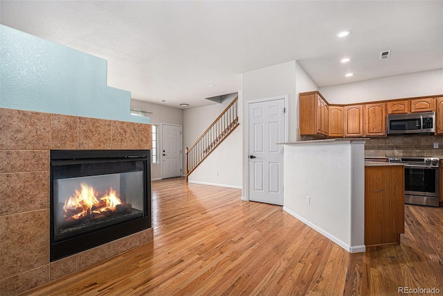 12710 Jasmine St Unit C, Thornton, CO 80602 - kitchen with brown cabinetry, wood finished floors, a fireplace, appliances with stainless steel finishes, and backsplash