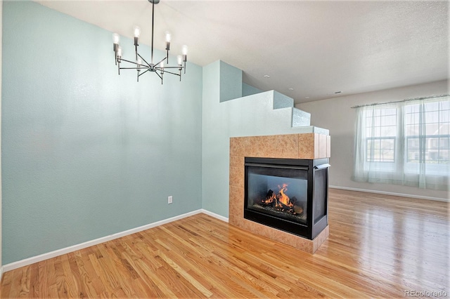 12710 Jasmine St Unit C, Thornton, CO 80602 - unfurnished living room with baseboards, wood finished floors, a notable chandelier, and a tiled fireplace