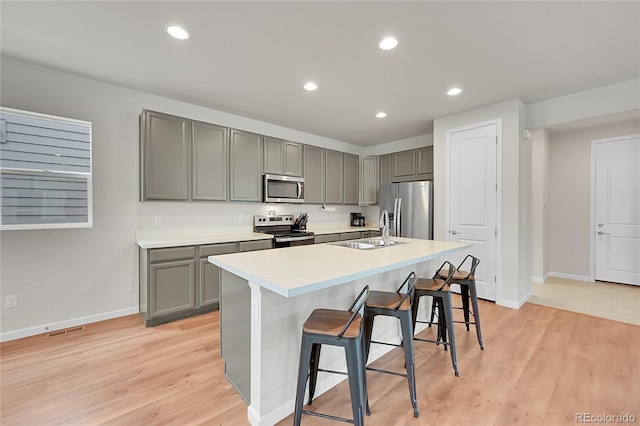 kitchen featuring a kitchen island with sink, a breakfast bar, a sink, light countertops, and appliances with stainless steel finishes