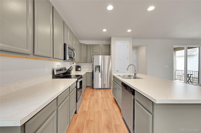 kitchen featuring stainless steel appliances, light countertops, a sink, and a center island with sink