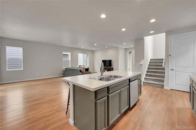 kitchen featuring a sink, open floor plan, light countertops, stainless steel dishwasher, and a center island with sink