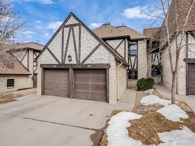 tudor home featuring driveway, a shingled roof, and brick siding