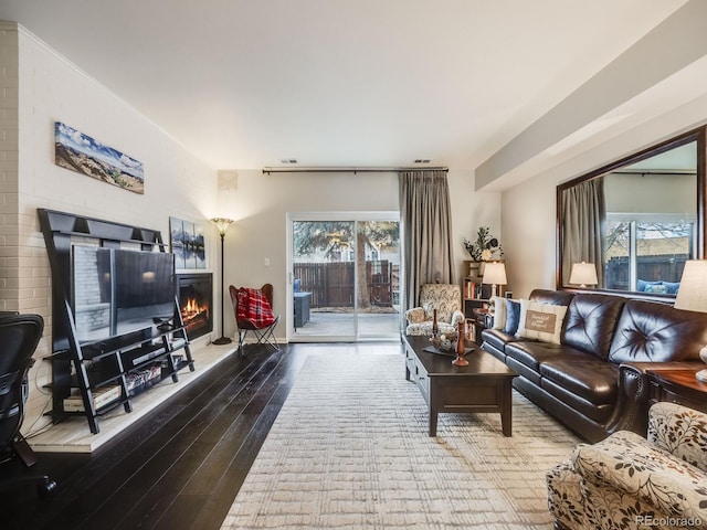 living area with visible vents, wood finished floors, a glass covered fireplace, and a wealth of natural light