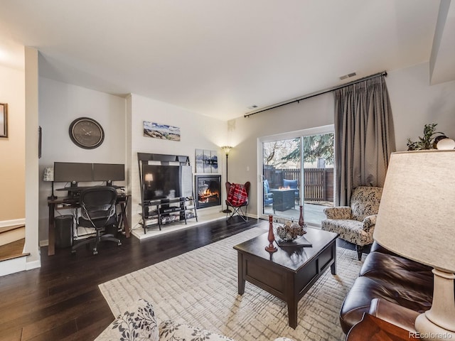 living room featuring wood finished floors, a glass covered fireplace, visible vents, and baseboards