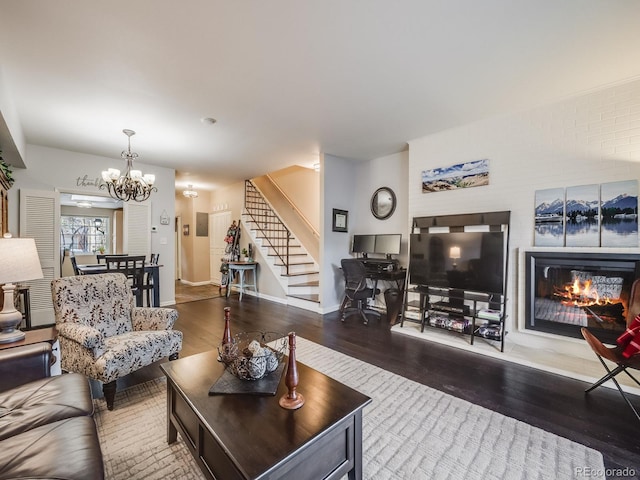 living room with a notable chandelier, stairway, a glass covered fireplace, wood finished floors, and baseboards