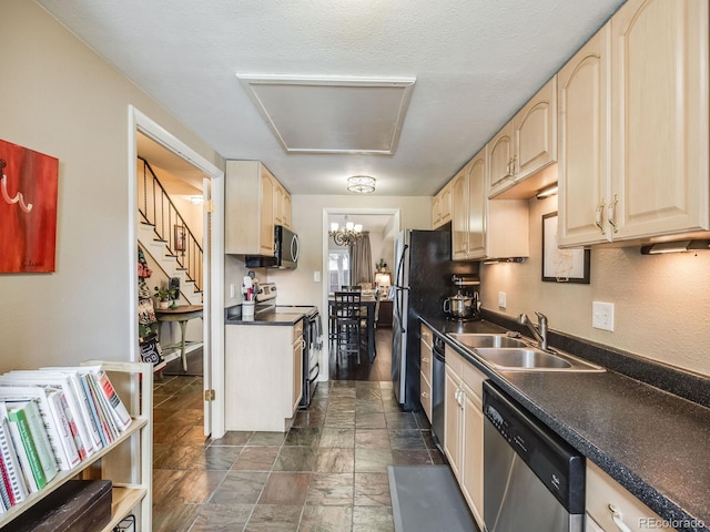 kitchen with light brown cabinets, a sink, appliances with stainless steel finishes, stone finish floor, and dark countertops