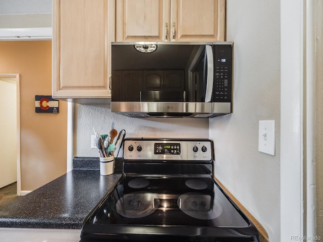 kitchen featuring stainless steel appliances, light brown cabinetry, and dark countertops