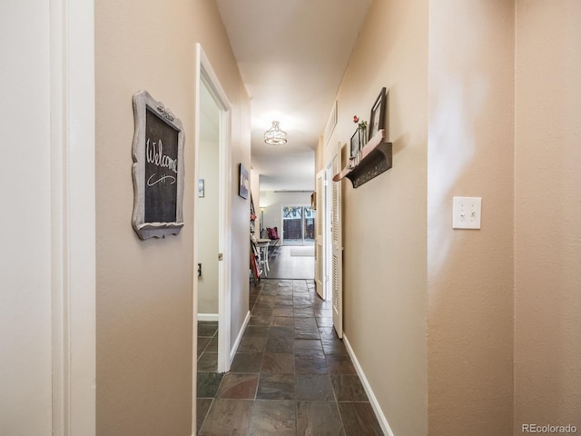 hall featuring stone tile floors and baseboards