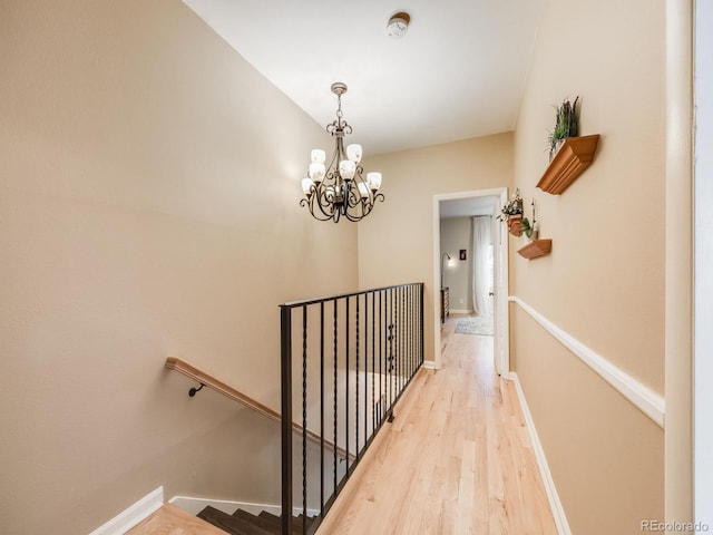 hall with light wood finished floors, baseboards, a chandelier, and an upstairs landing