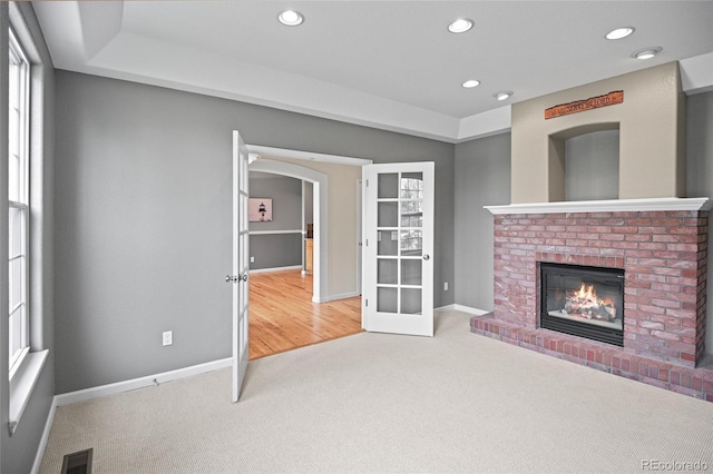 unfurnished living room featuring a fireplace, french doors, and carpet