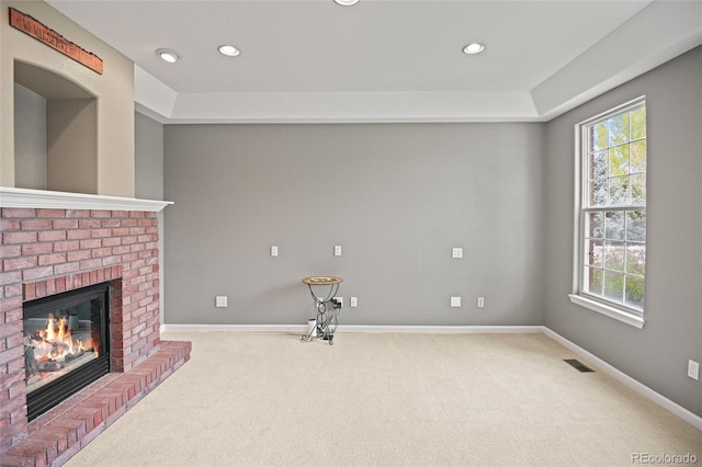 unfurnished living room with a brick fireplace, light carpet, and a healthy amount of sunlight