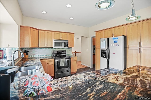 kitchen featuring pendant lighting, tasteful backsplash, appliances with stainless steel finishes, dark stone countertops, and sink