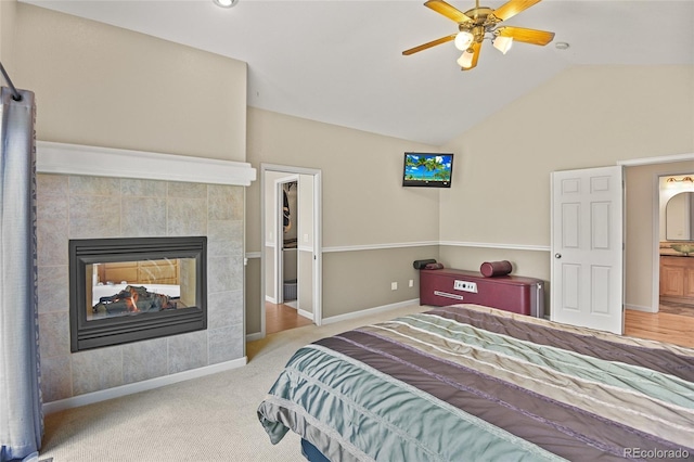 carpeted bedroom with lofted ceiling, ensuite bath, a tiled fireplace, and ceiling fan