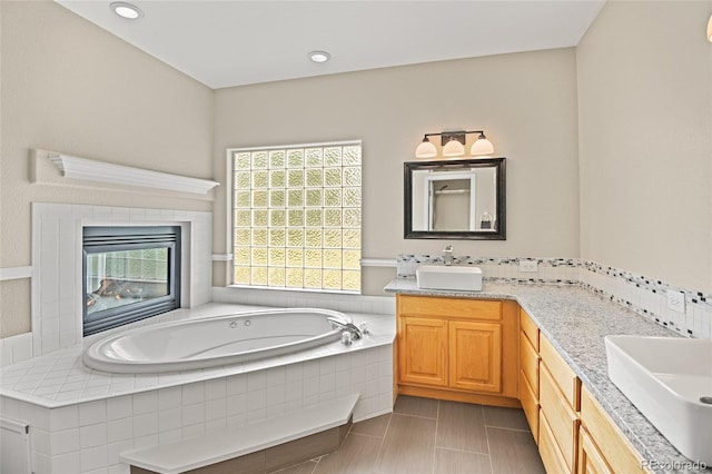 bathroom with a fireplace, a relaxing tiled tub, and vanity