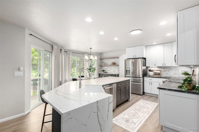 664 Clarendon Dr, Longmont, CO 80504 - kitchen with stainless steel appliances, a center island with sink, backsplash, light wood finished floors, and recessed lighting