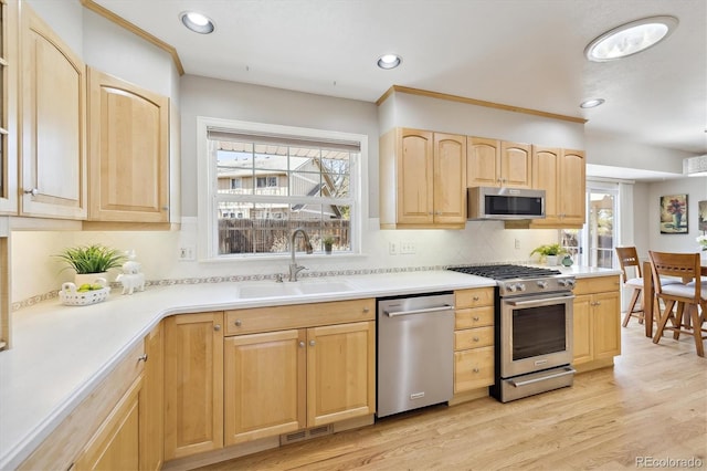 kitchen with light brown cabinets, a sink, light wood-style floors, appliances with stainless steel finishes, and light countertops