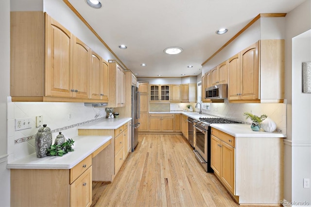 kitchen featuring tasteful backsplash, light countertops, appliances with stainless steel finishes, light wood-style floors, and a sink