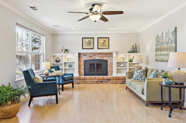 living room with visible vents, a brick fireplace, ornamental molding, wood finished floors, and a ceiling fan