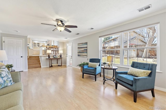 living area featuring crown molding, light wood-style floors, visible vents, and baseboards