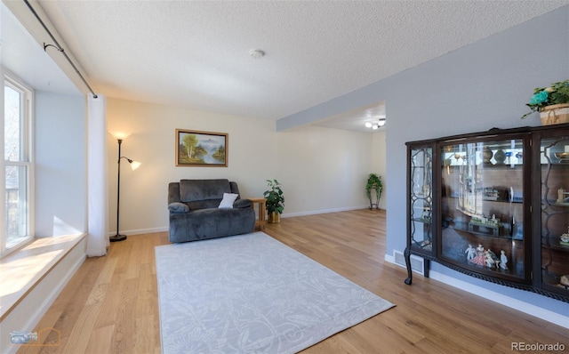 living area featuring a textured ceiling, light wood-type flooring, visible vents, and baseboards