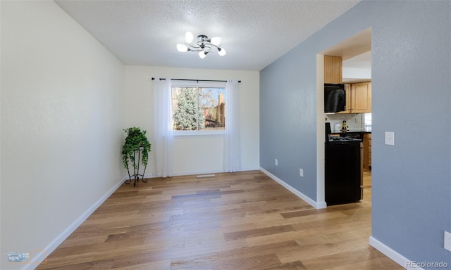 unfurnished dining area featuring a textured ceiling, baseboards, an inviting chandelier, and light wood-style floors