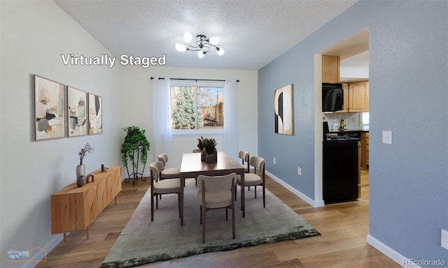 dining area featuring a textured ceiling, light wood finished floors, baseboards, and an inviting chandelier