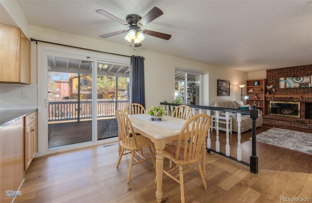 dining room featuring light wood-style floors, a brick fireplace, and a textured ceiling