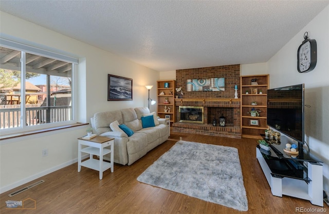 living area featuring a brick fireplace, a textured ceiling, visible vents, and wood finished floors