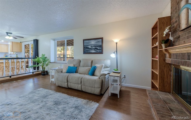 living area featuring a fireplace, a textured ceiling, baseboards, and wood finished floors