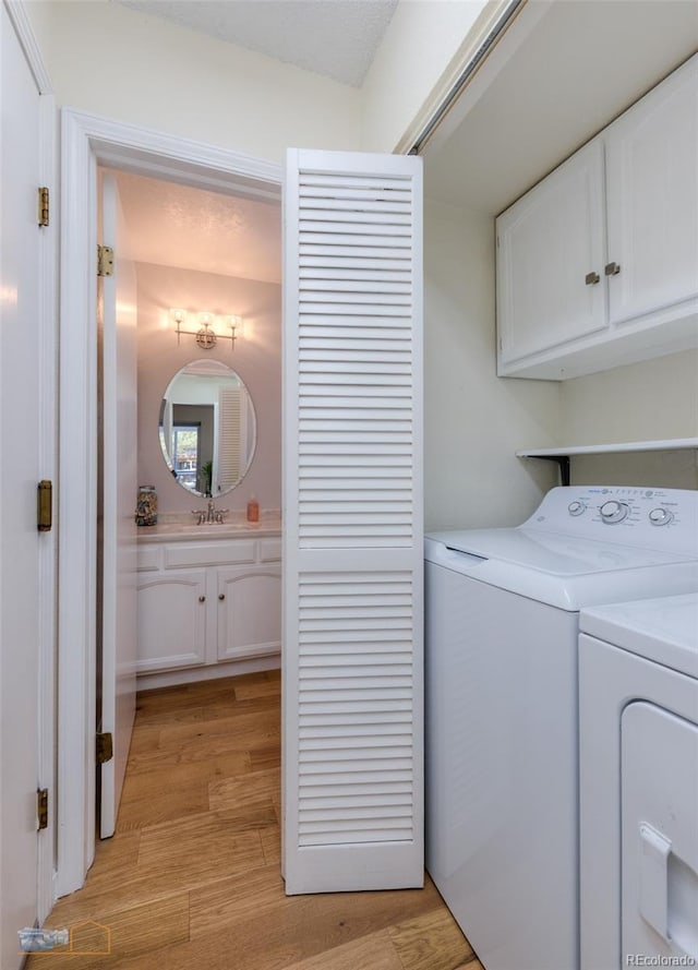 laundry room featuring cabinet space, washing machine and dryer, light wood-style flooring, and a sink