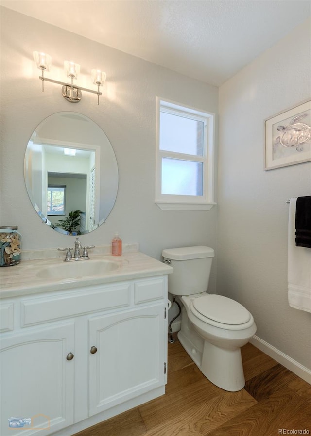 half bath featuring toilet, a wealth of natural light, wood finished floors, and vanity