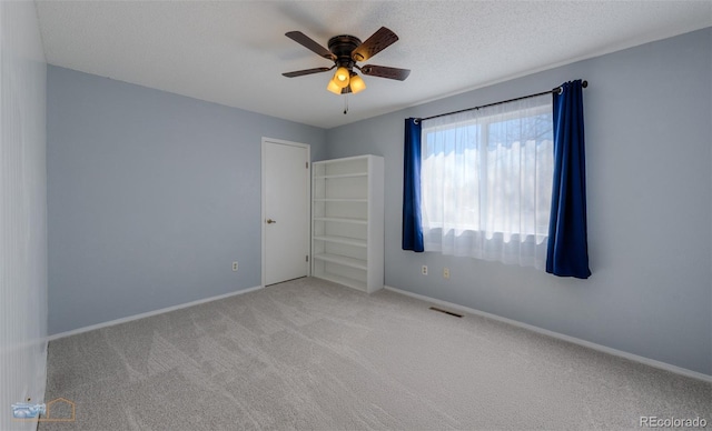 carpeted spare room with a textured ceiling, a ceiling fan, visible vents, and baseboards