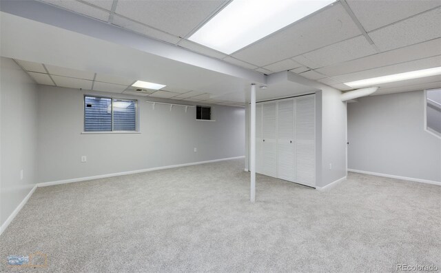 finished basement featuring carpet flooring, a paneled ceiling, and baseboards