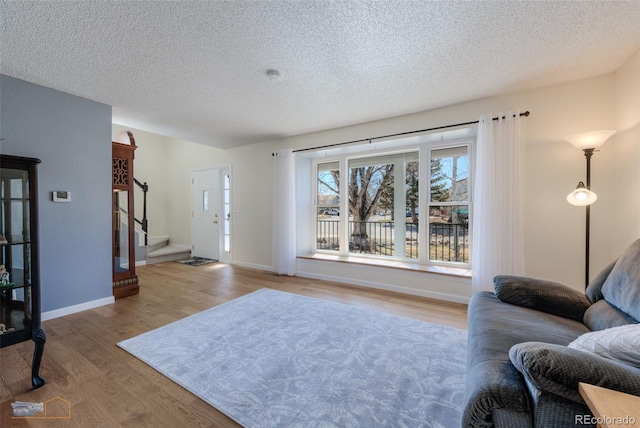 living area with stairs, a textured ceiling, wood finished floors, and baseboards