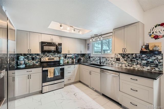 kitchen with a sink, dark countertops, marble finish floor, and stainless steel appliances